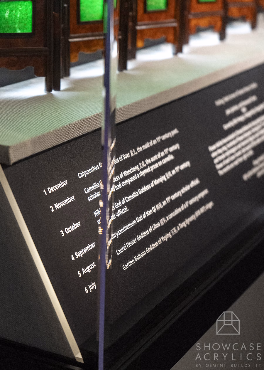 Close-up of a display panel with a left column listing months and a right column of text, separated by a vertical glass divider, in a museum exhibit.