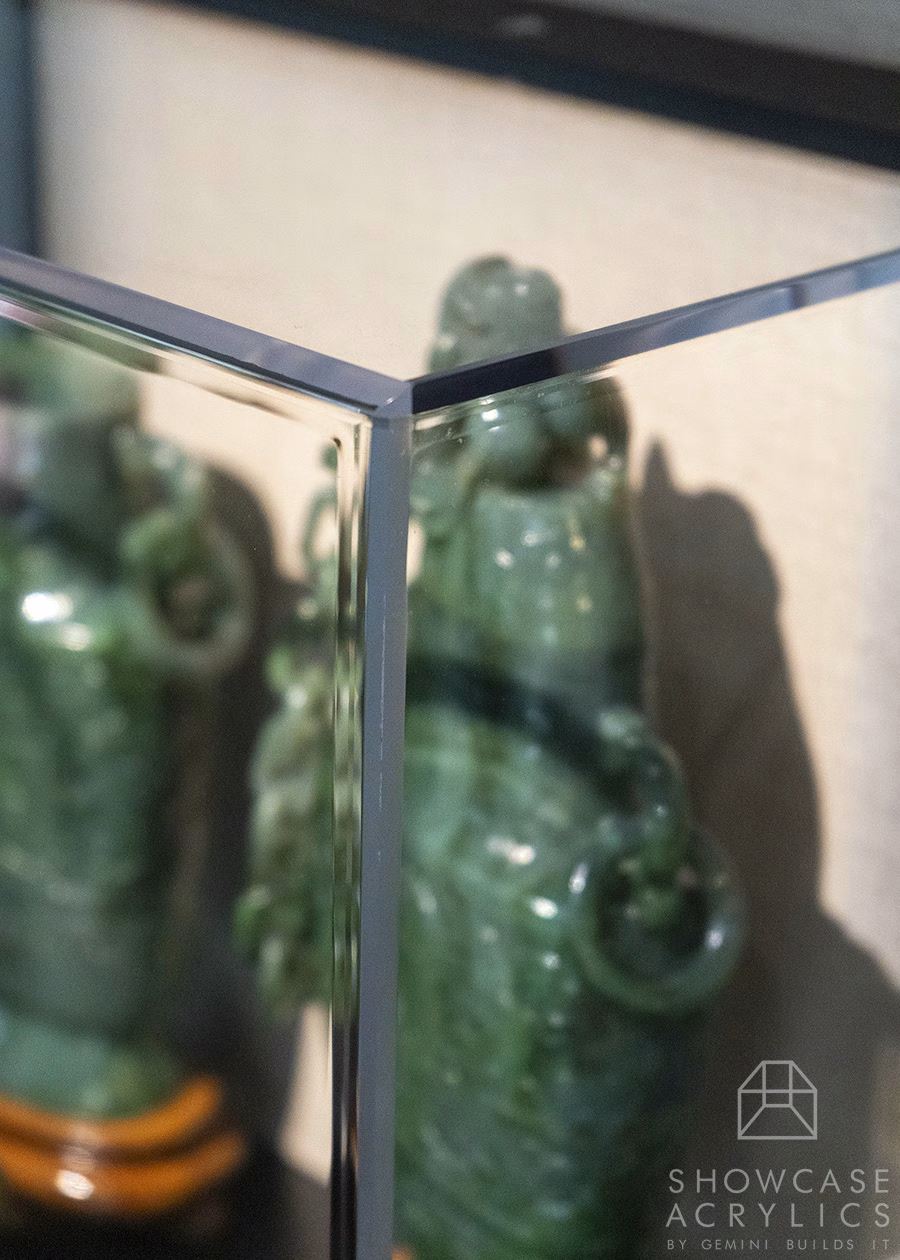 Corner of a glass display case with green glazed ceramic bottles inside, reflections visible on the glass surface.